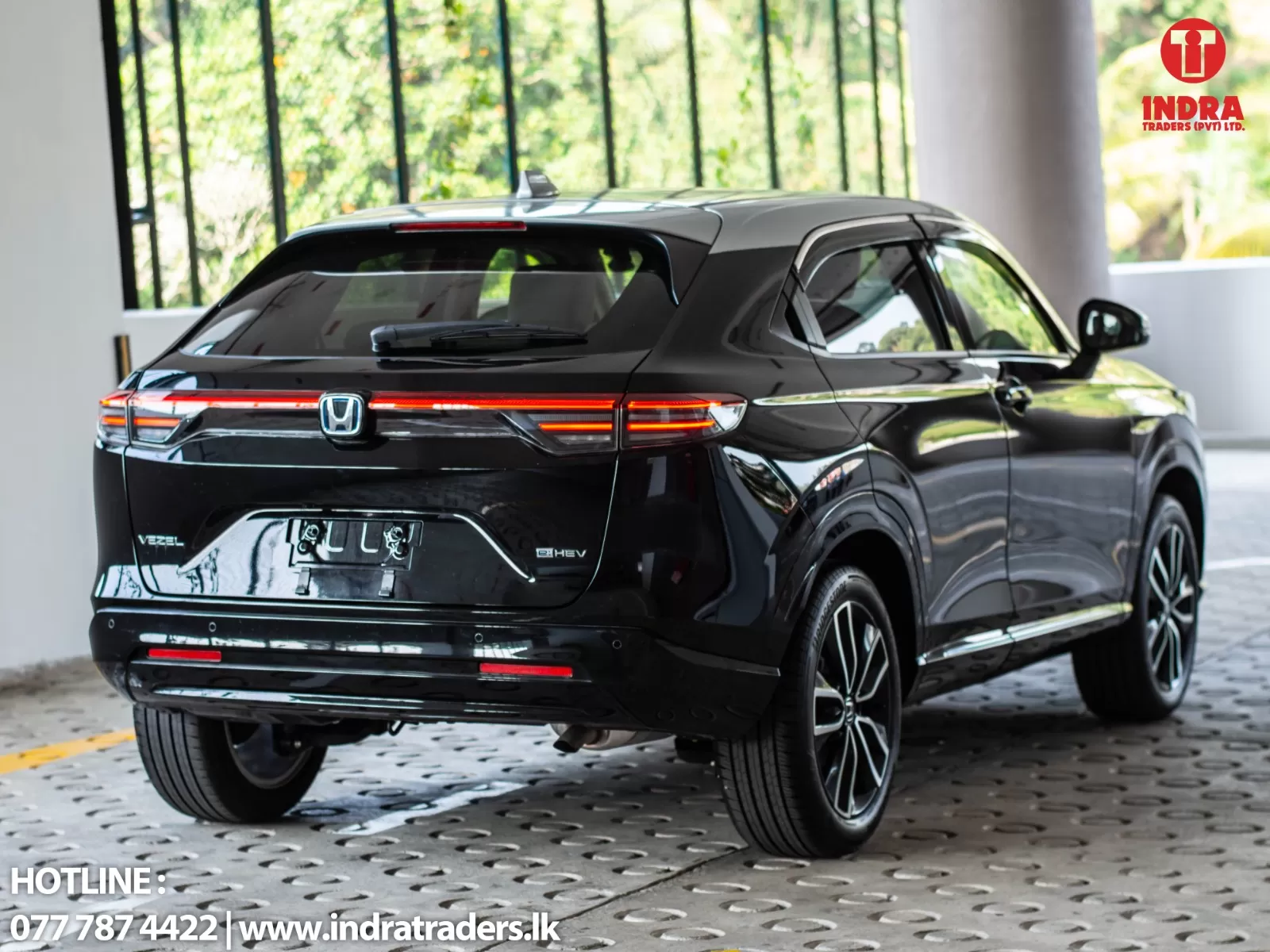 Rear three-quarter view of a black Honda Vezel e:HEV SUV parked indoors, with red LED tail lights and showroom logo in the top-right corner.
