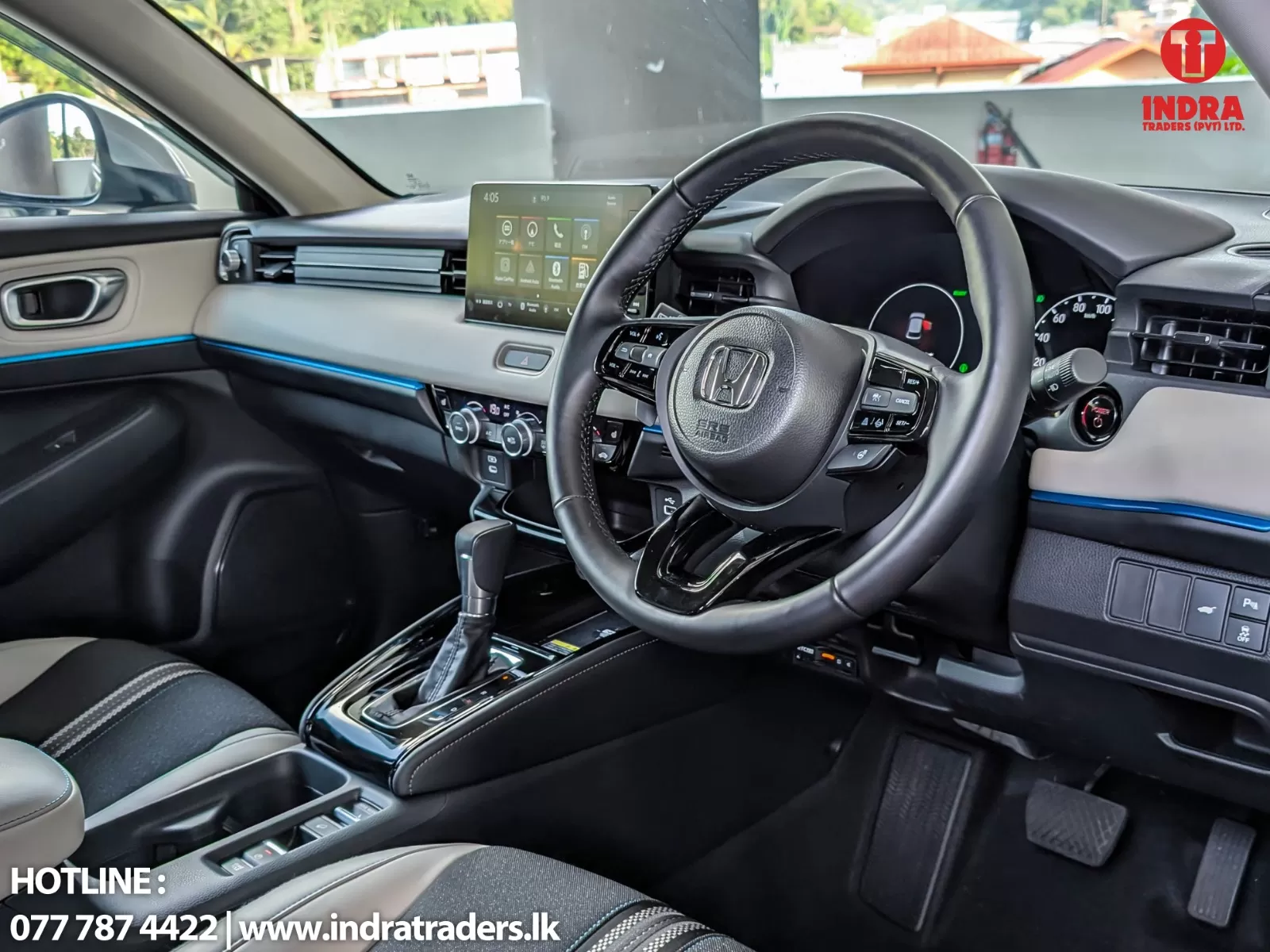 Modern car interior showing steering wheel, central touchscreen, gear shifter, and blue ambient trim; logo visible on windshield area.