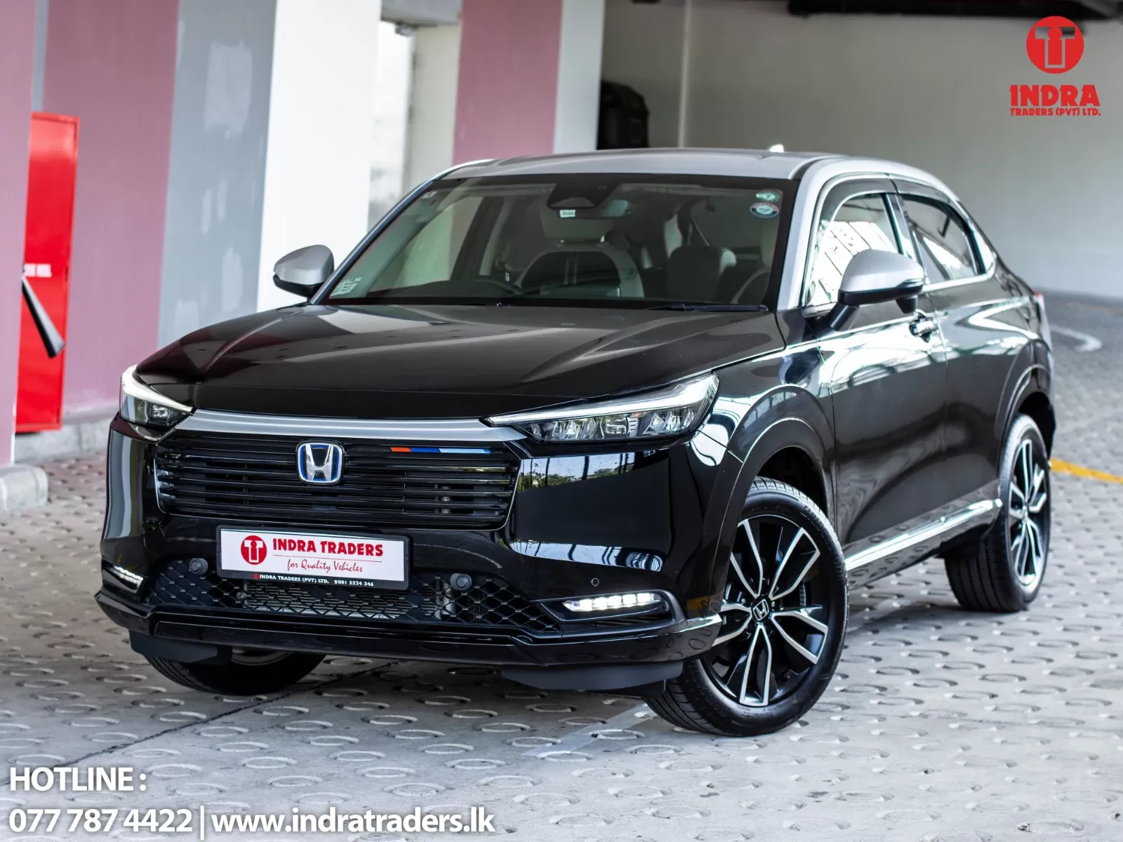 Black Honda SUV shown from a front three-quarter angle inside a showroom, with chrome grille, sleek LED headlights, and large alloy wheels; Indra Traders branding appears on the license plate and in the upper-right corner.
