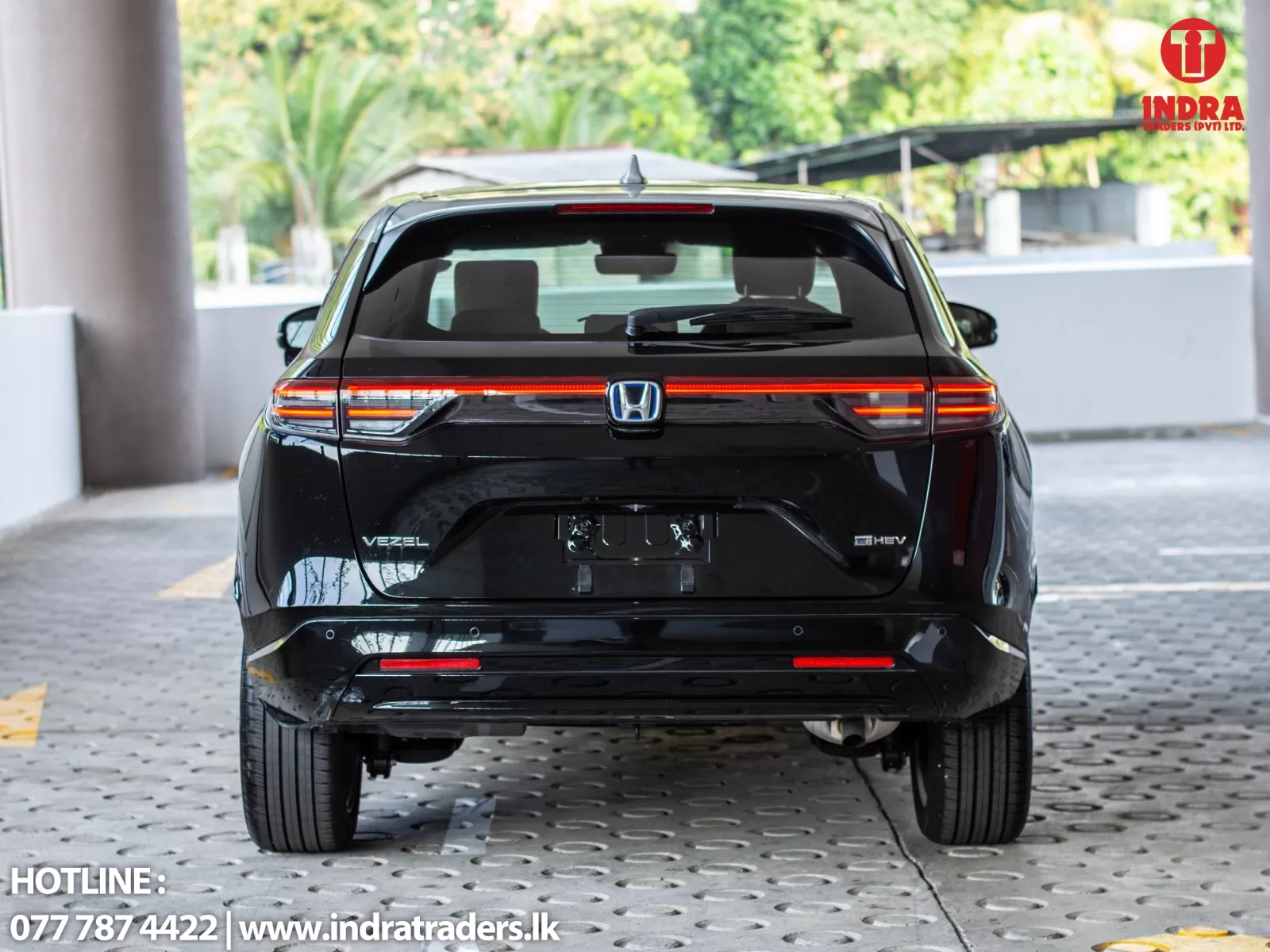 Rear view of a black Honda Vezel HEV SUV with red LED taillights, parked on a perforated concrete surface; dealership logo in top-right corner.