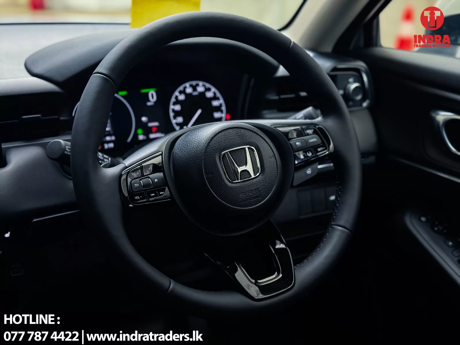 Close-up of a Honda steering wheel and dashboard with the Indra Traders logo in the top-right corner and hotline text at the bottom left.