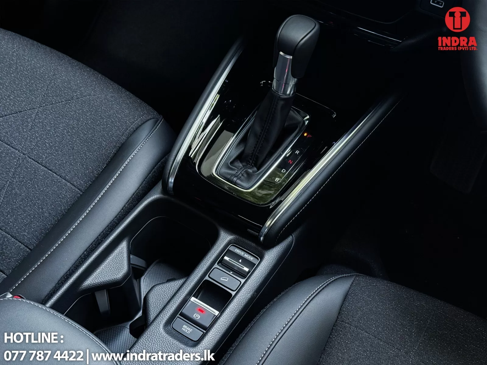 Close-up of a car's center console with an automatic gear lever and glossy trim; INDRA Traders logo in the top-right.