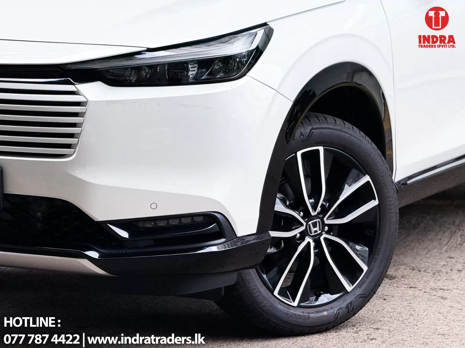 Close-up of a white car's front end showing the headlight, grille, and stylish alloy wheel with the Indra Traders logo in the corner.