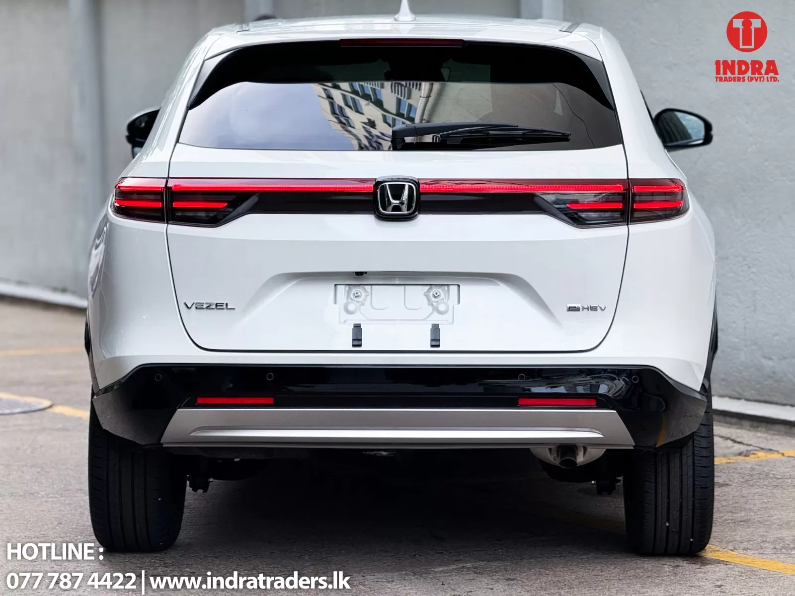 Rear view of a white Honda Vezel e:HEV SUV with red taillights, parked outdoors; Indra Traders logo in the top-right corner