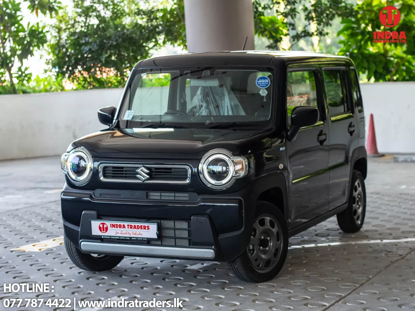 Front-left view of a black Suzuki compact SUV with round headlights and chrome grille, parked in a showroom area with Indra Traders branding in the corner.