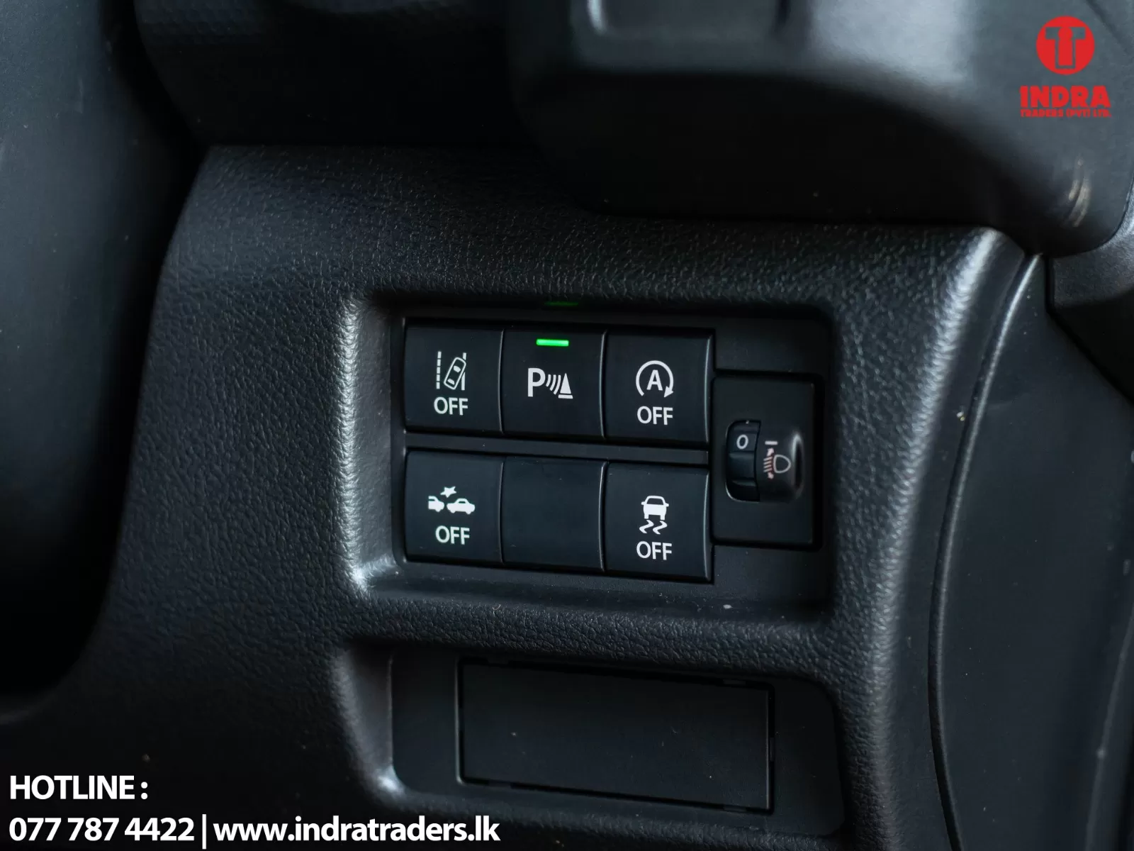 Close-up of a car's center dashboard panel with OFF switches for lane departure warning, parking sensors (green indicator), auto start/stop, and traction control; headlight level dial on the right.
