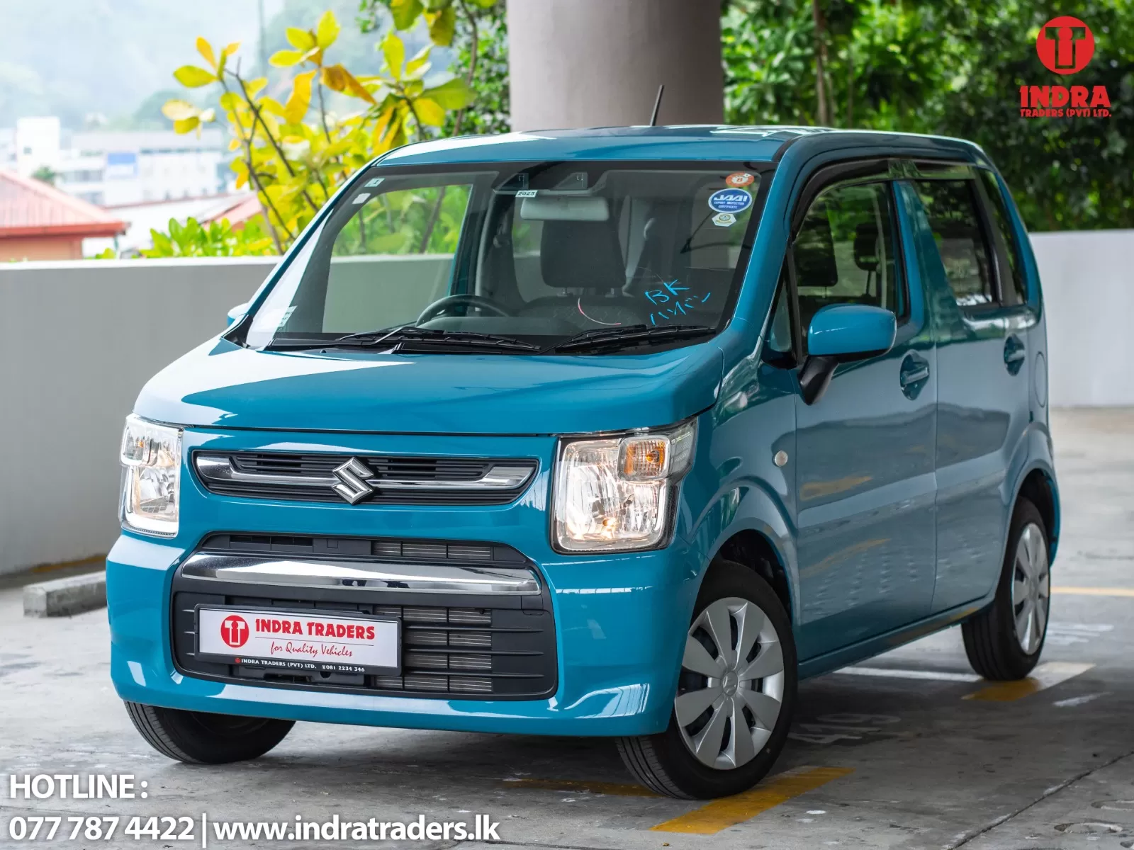 Blue Suzuki van shown in a parking area, front three-quarter view with Indra Traders branding on the license plate and logo in the top-right corner of the image