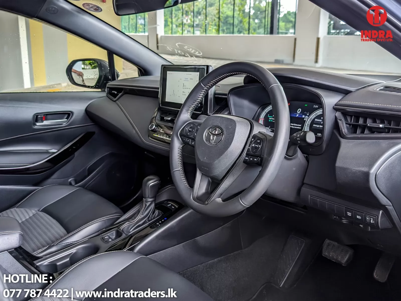 Interior view of a modern car: steering wheel, center touchscreen, gear shifter, and black leather seats with white stitching.