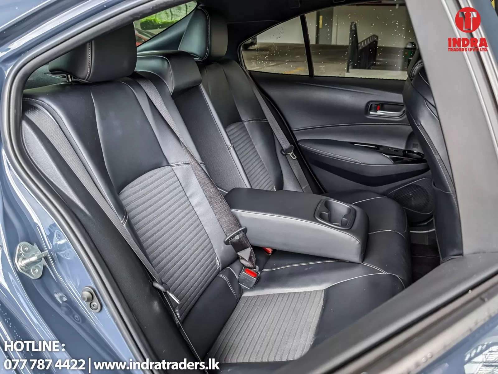 Rear passenger area of a dark sedan with black leather seats and gray fabric inserts; center armrest with cup holder, seat belts visible, window with rain droplets.