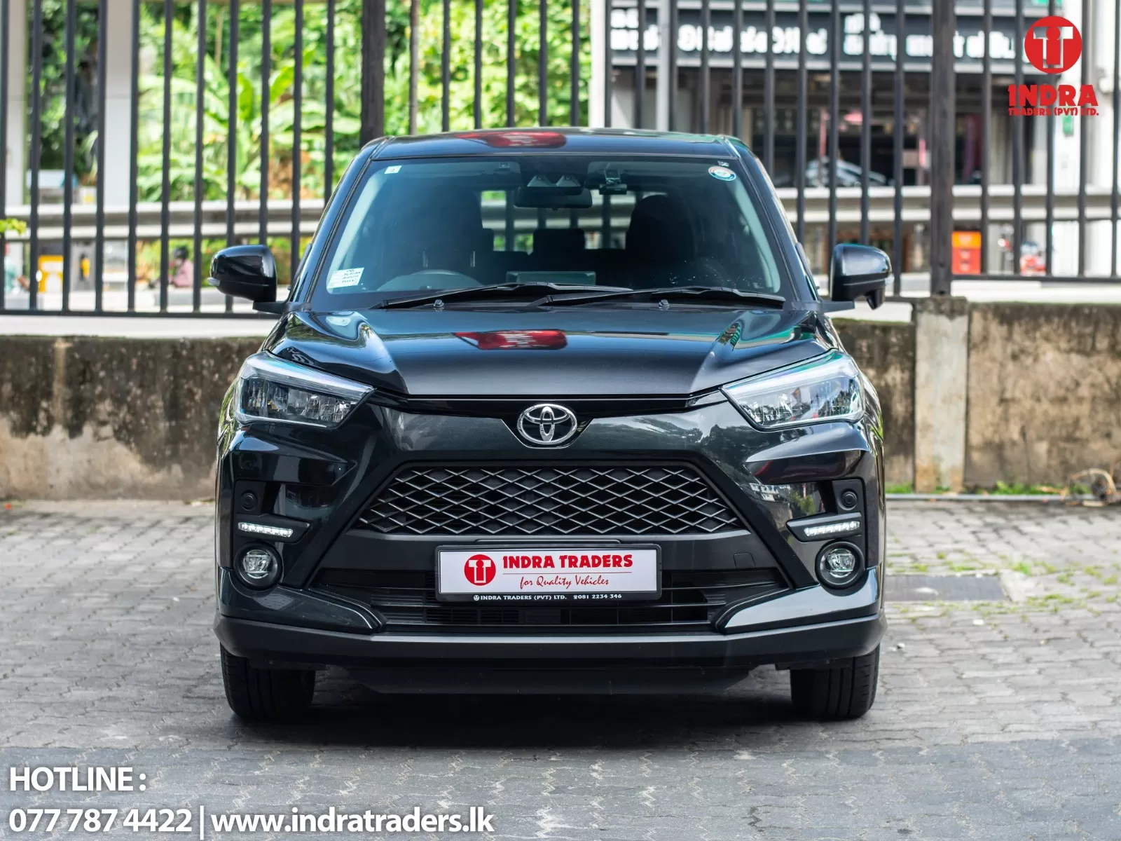 Front view of a dark gray Toyota SUV parked on a paved area with a dealership logo in the top-right corner and contact text at the bottom left.