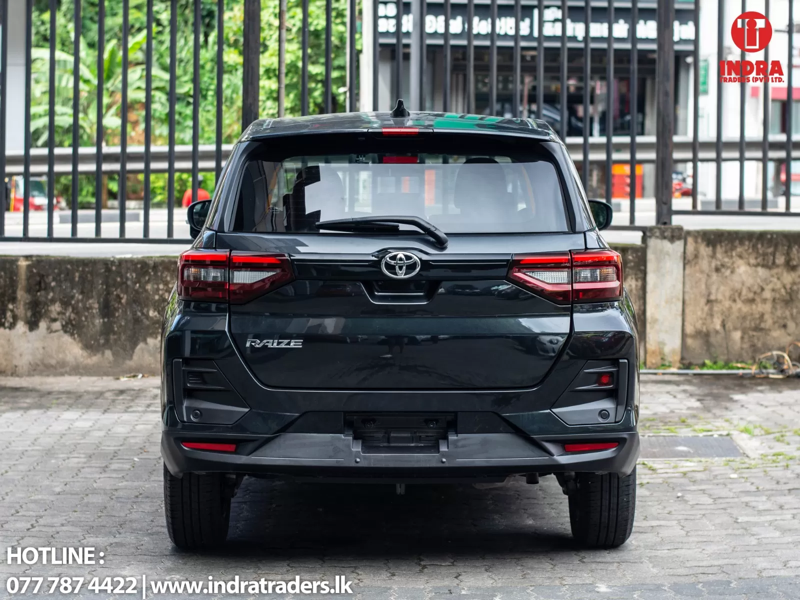 Rear view of a dark gray Toyota Raize SUV parked in a lot; taillights visible and dealership branding in the background.