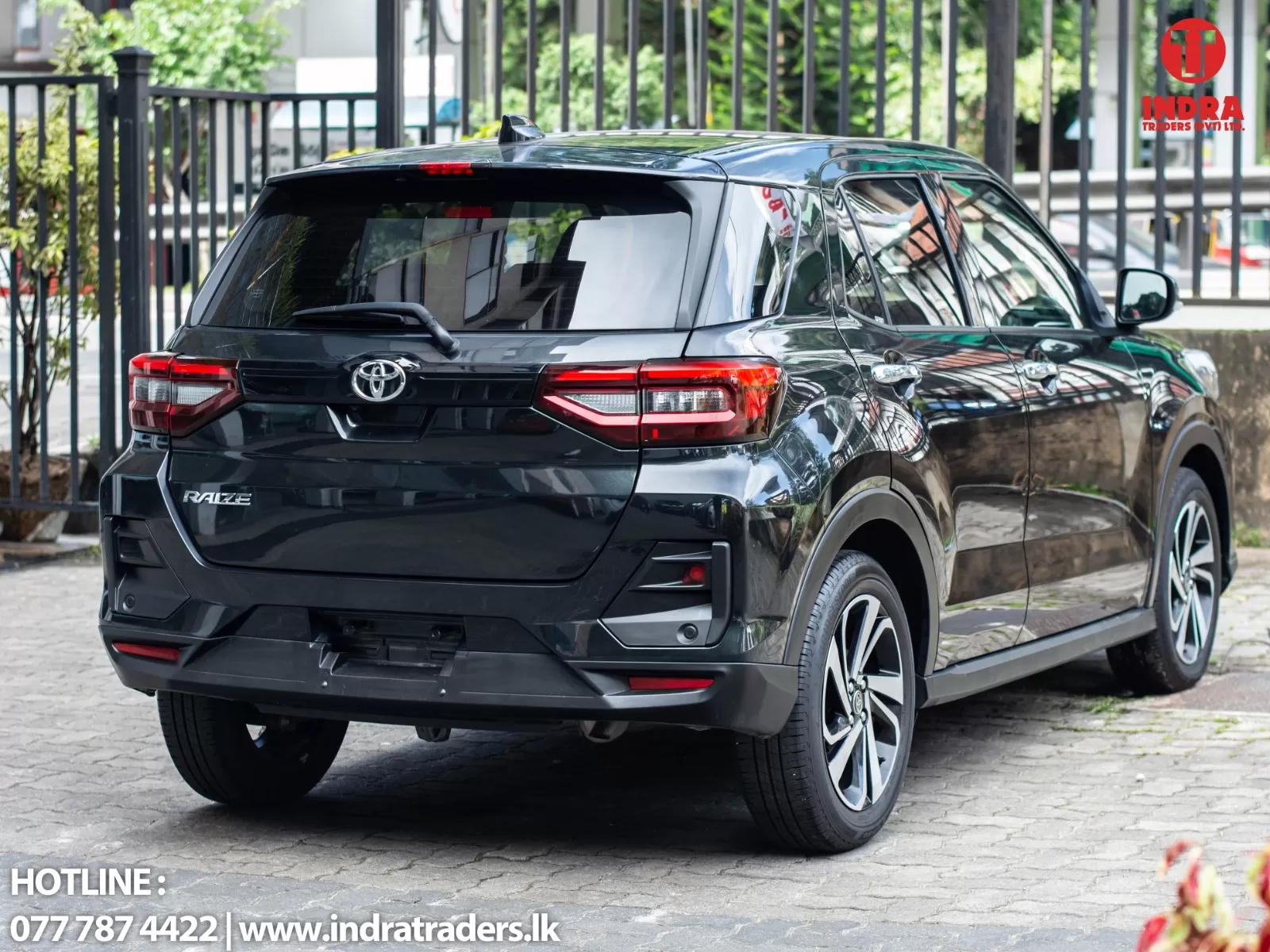 Rear three-quarter view of a glossy black Toyota Raize SUV parked on a cobblestone street; dealership watermark 'INDRA TRADERS' in the top-right.