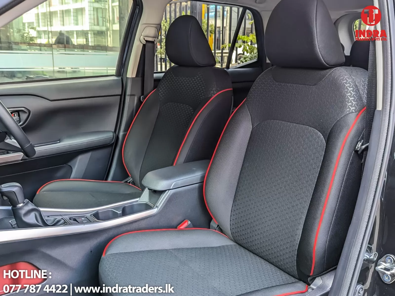 Front car seats with black fabric and red piping, center console and gear lever visible inside a showroom-set vehicle.