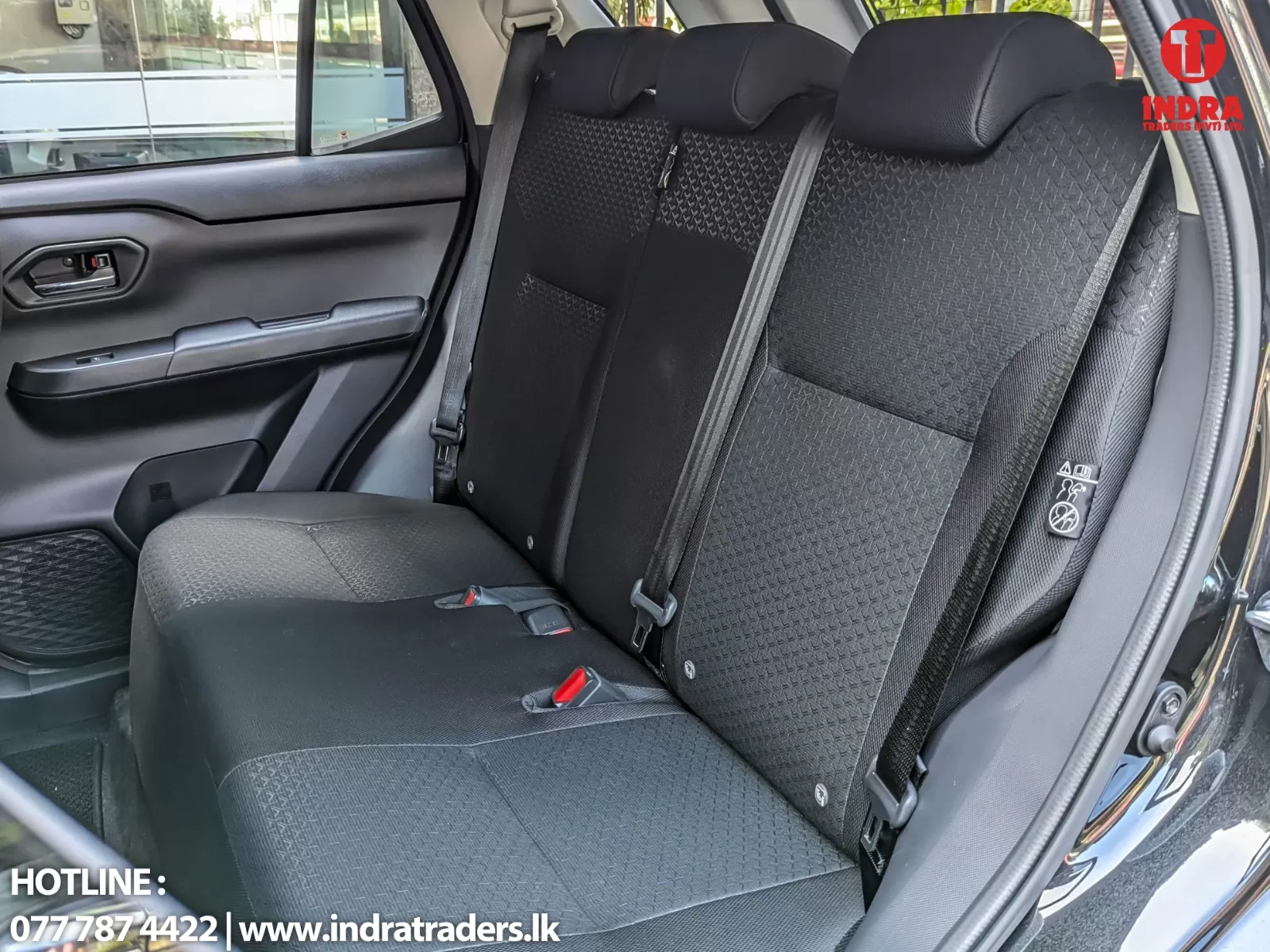 Rear row of a black car interior with three seats, headrests, and visible seat belts; Indra Traders logo appears in the top-right corner.