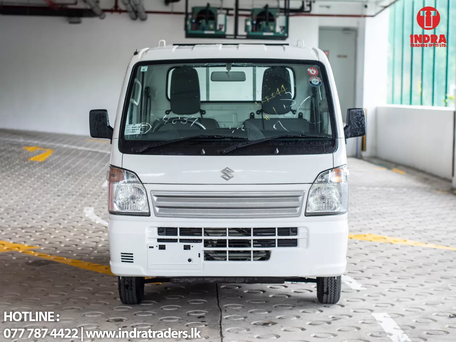 Front view of a white compact van parked in a showroom, Indra Traders logo in the top-right corner and contact details at the bottom left.