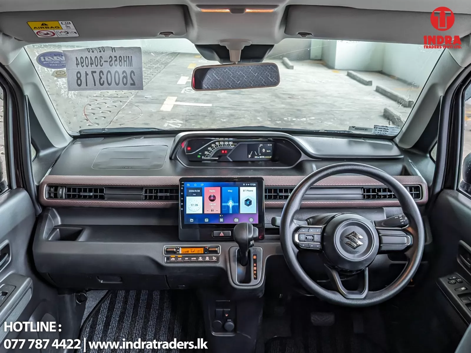 Right-hand drive car interior with a large touchscreen infotainment screen, digital instrument cluster, steering wheel, and rearview mirror; Indra Traders logo in the corner.