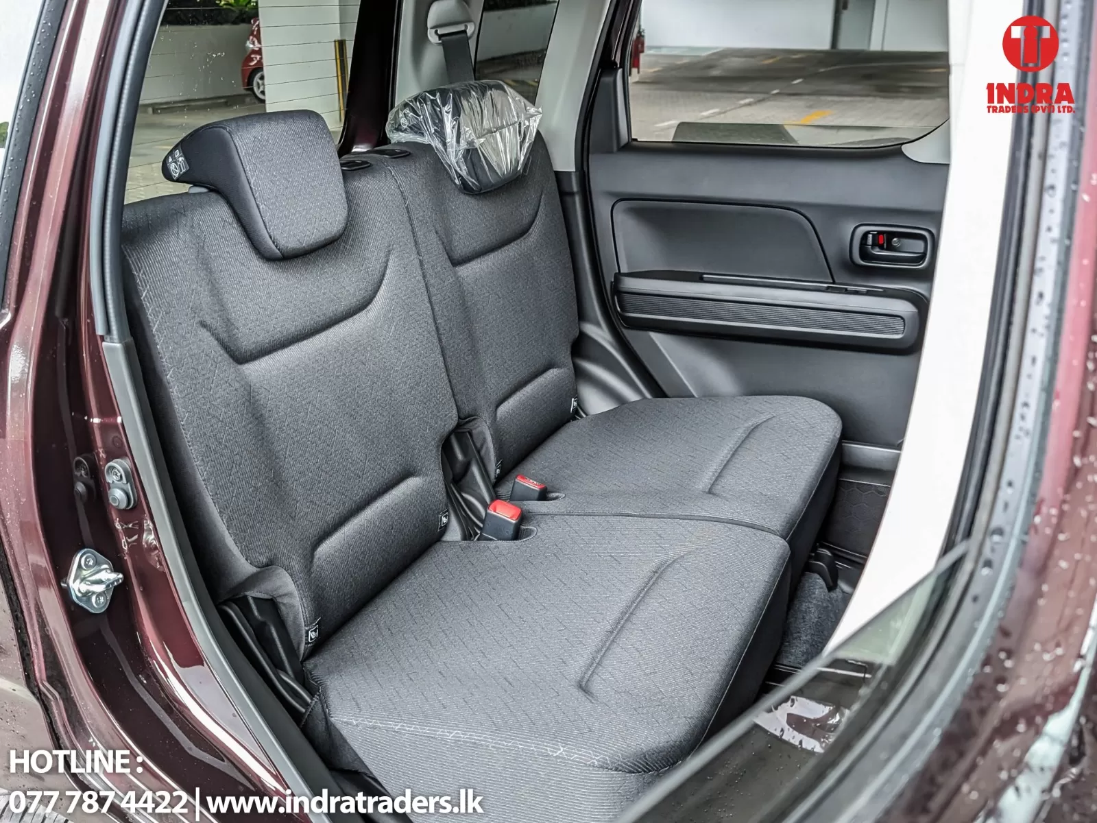 Rear interior of a car: gray fabric bench seats with headrests, door panel, and window visible inside a maroon vehicle.