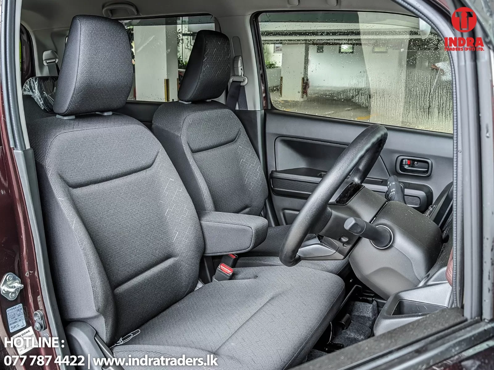 Interior of a car front cabin with driver and passenger seats, steering wheel, and rainy side window visible.