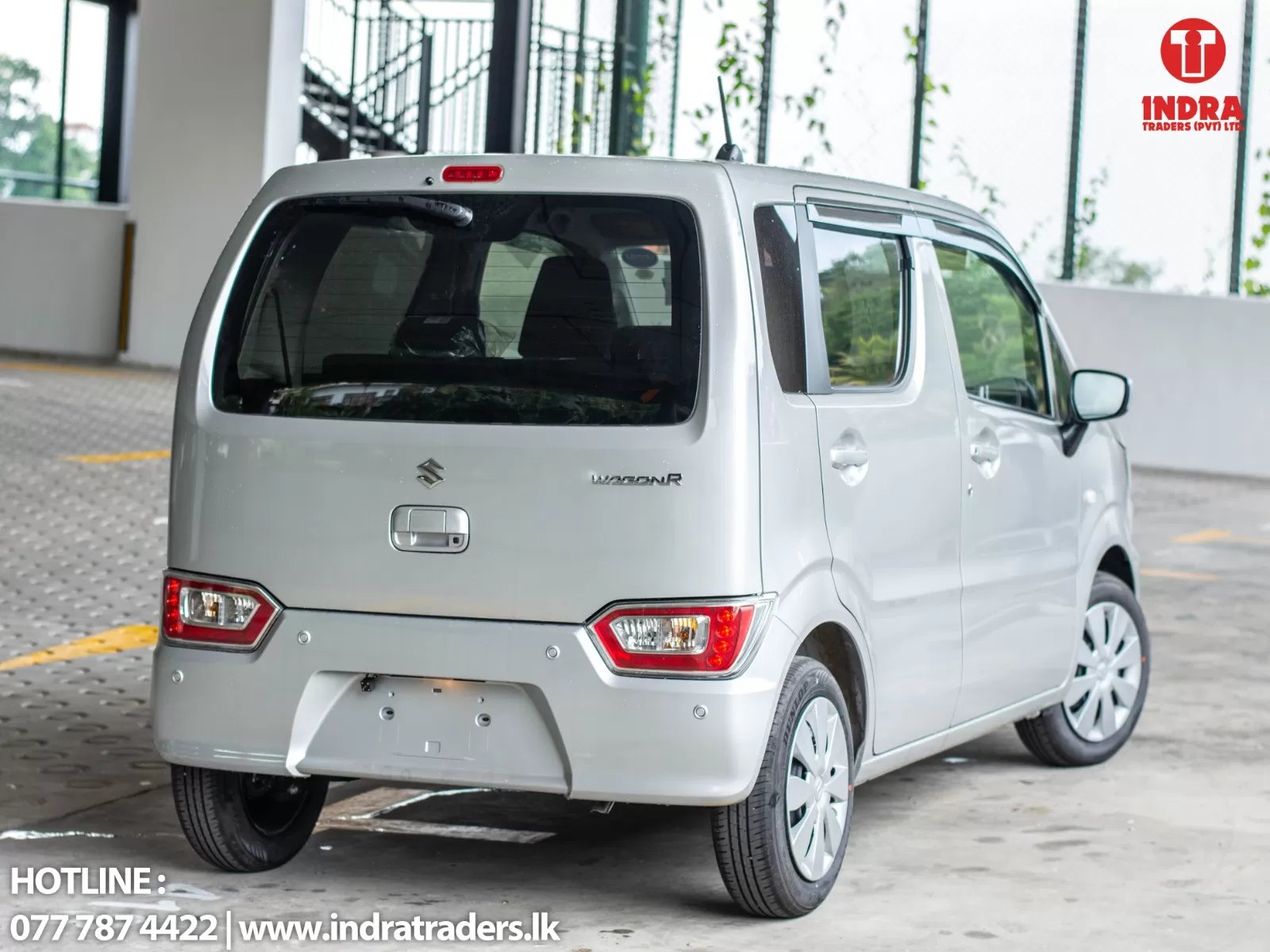 Rear three-quarter view of a white Suzuki WagonR parked in a lot; Indra Traders logo in the top-right and contact text at bottom-left.