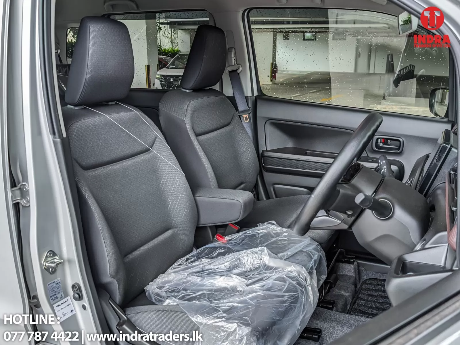 Front cabin of a vehicle showing gray cloth seats, plastic seat covers, steering wheel, and raindrop-speckled windows on a cloudy day.