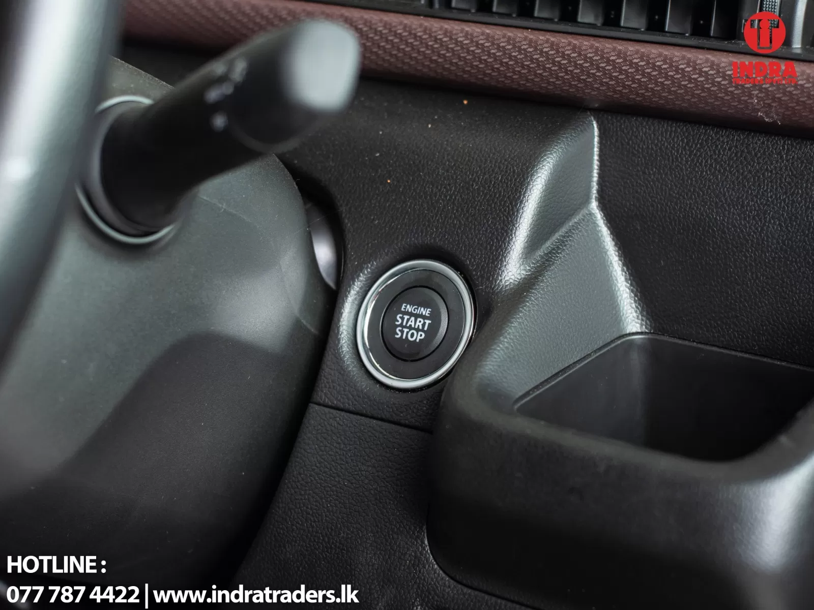 Close-up of a car's engine start/stop button in a black, textured dashboard with the INDRA Traders logo in the corner of the image
