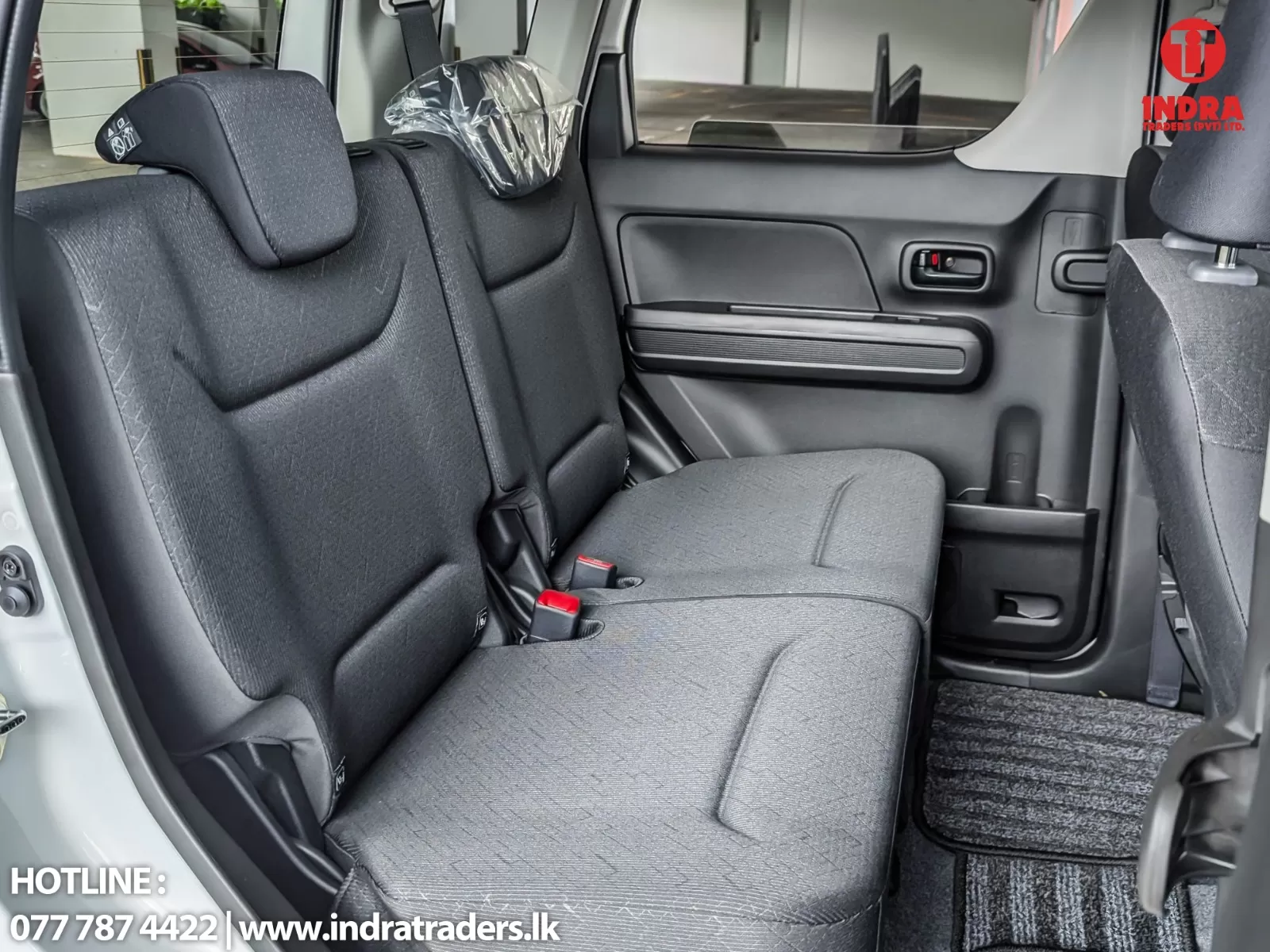 Rear car interior with two dark fabric seats, headrests, and a door panel; red seatbelt buckles visible.