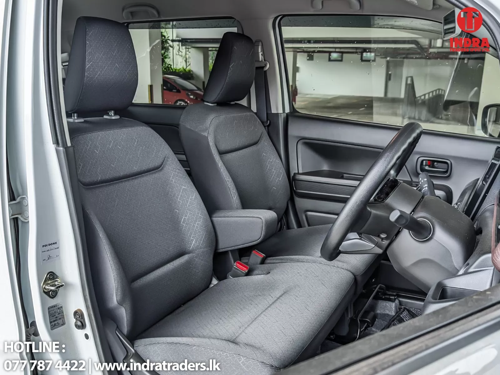 Interior of a right-hand-drive vehicle showing front seats, steering wheel, and open driver door in a showroom.