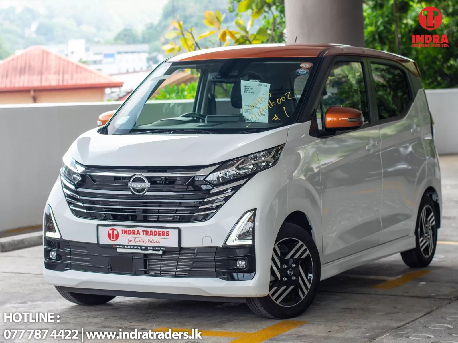 White Nissan van with orange mirrors parked in a lot, branded with Indra Traders on the front plate area and a red Indra logo in the top-right corner.