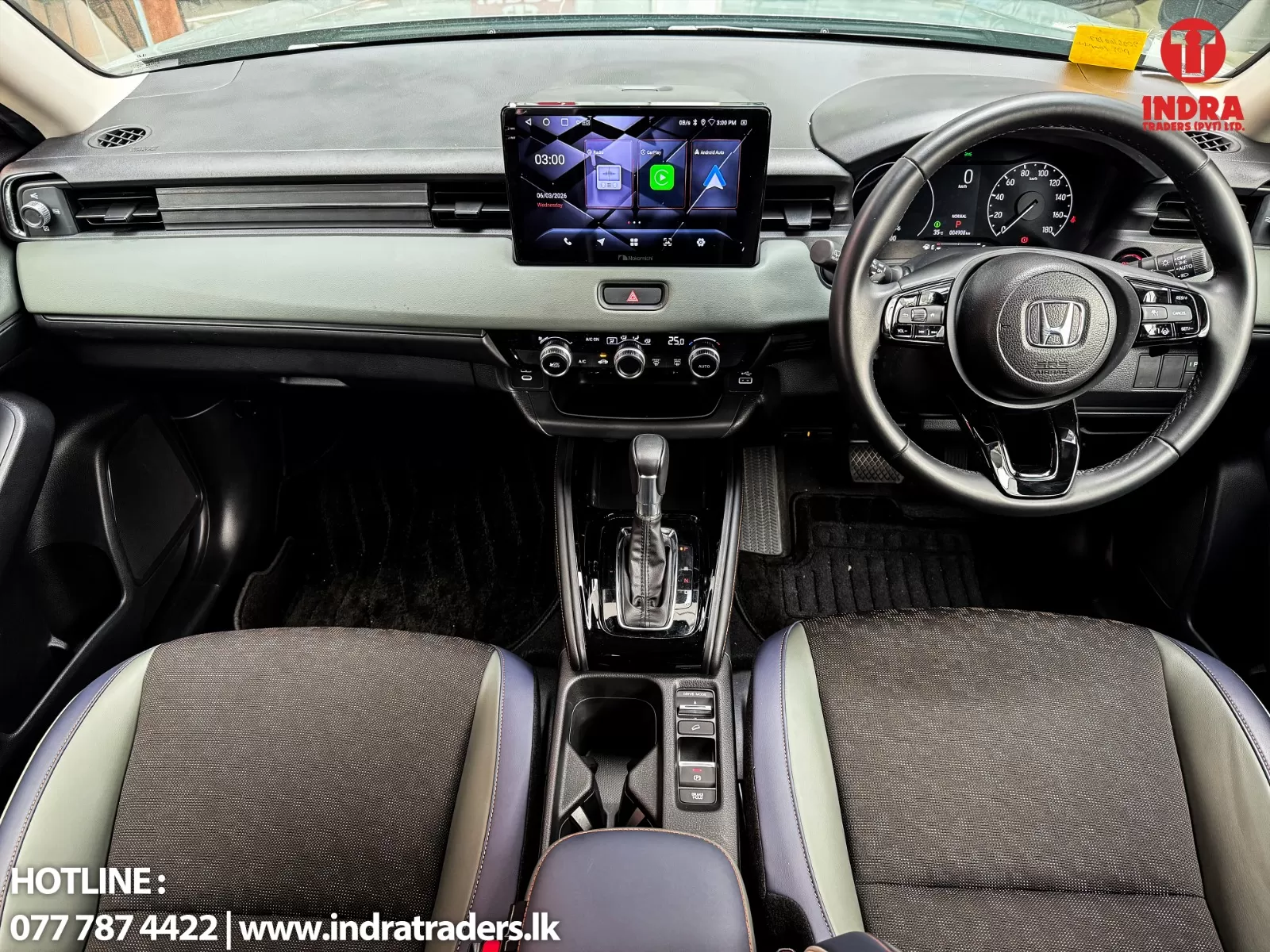 Interior view of a Honda car dashboard with a central touchscreen, steering wheel, and gear selector visible, showroom-style lighting.