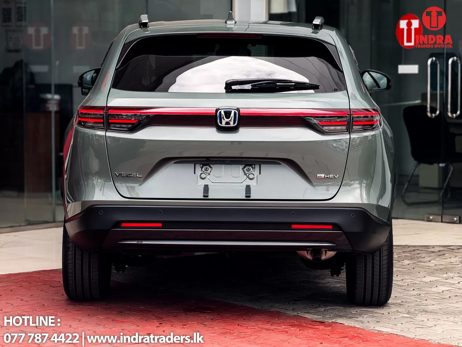 Rear view of a silver Honda Vezel eHEV SUV in front of a showroom, with red taillights and a tinted rear window.