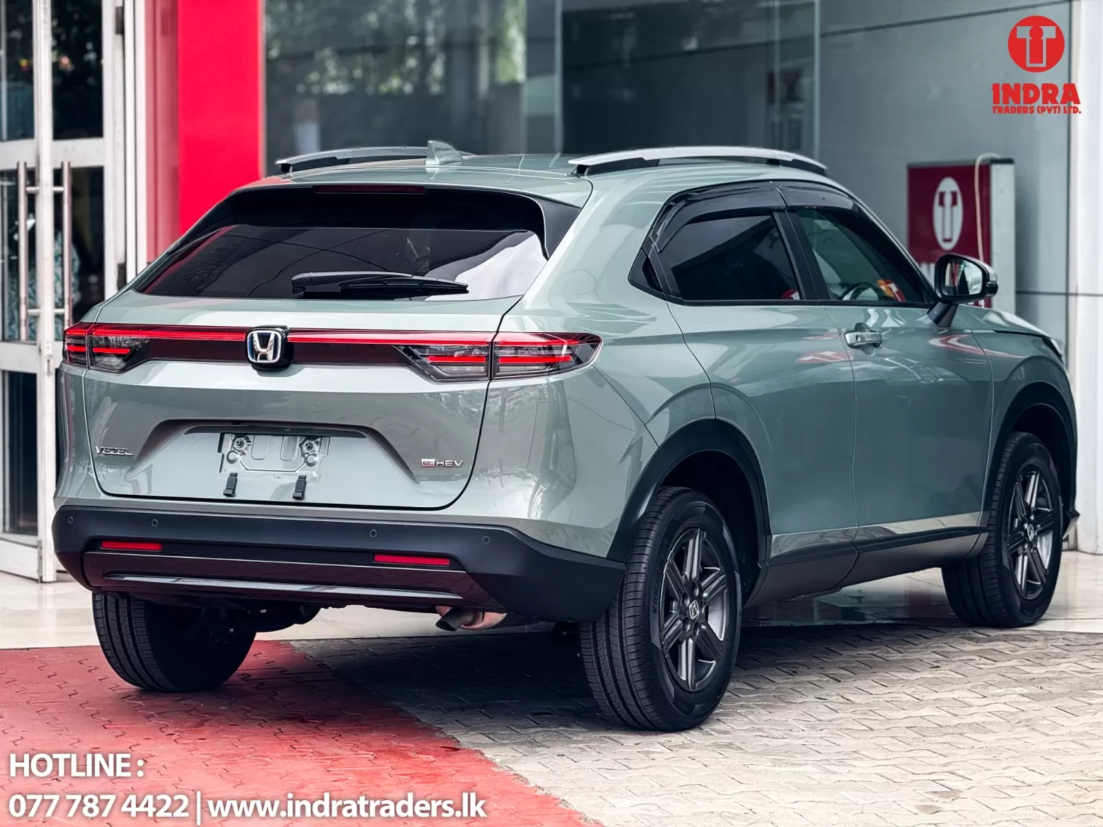 Rear three-quarter view of a silver Honda Vezel SUV at a dealership, with Indra Traders logo in the corner.