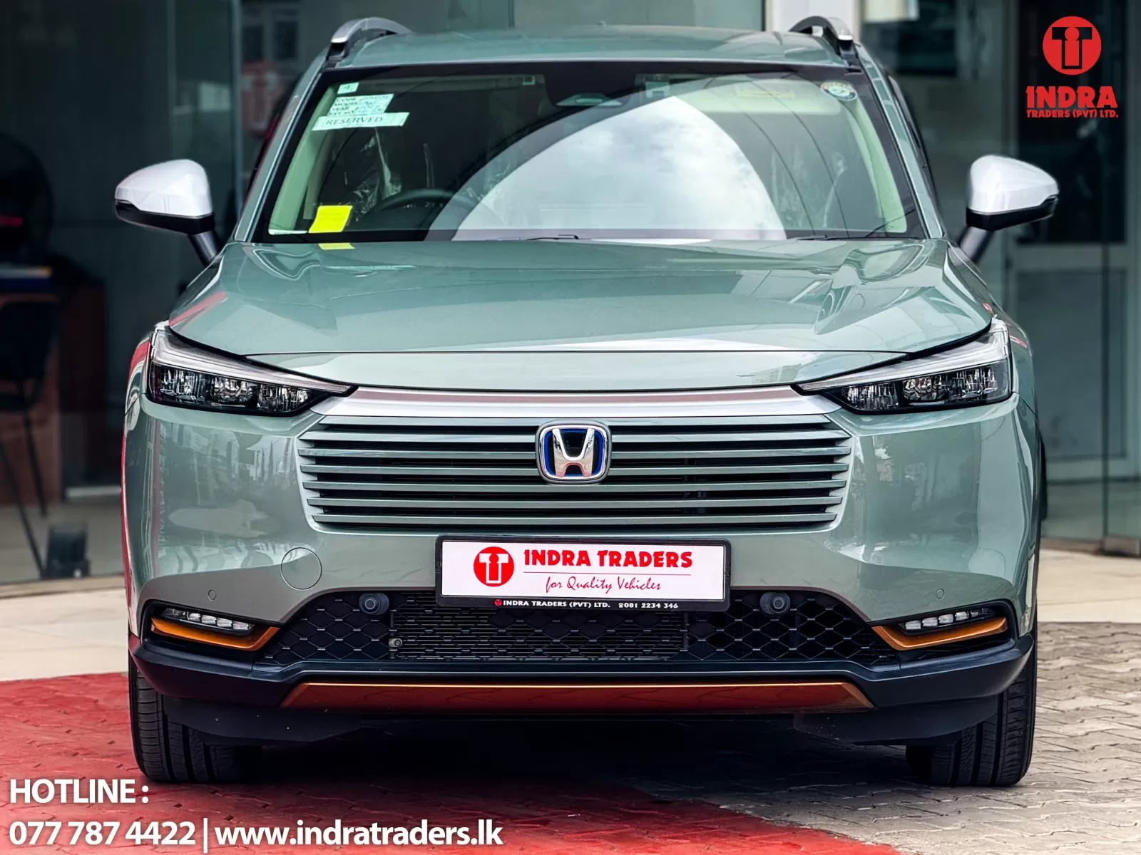 Front view of a silver Honda SUV at a dealership, with Indra Traders branding on the license plate and logo in the corner.