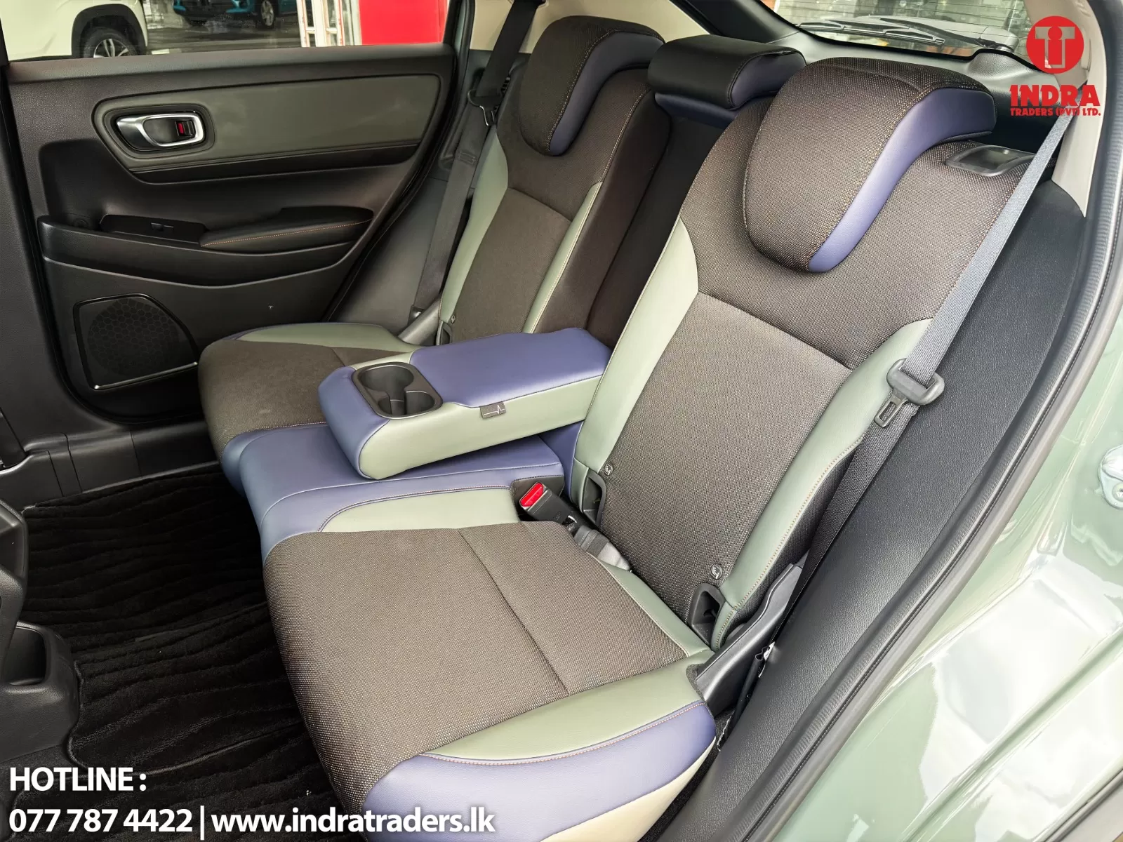 Rear car seats with multicolored upholstery and a fold-down center armrest containing two cupholders.