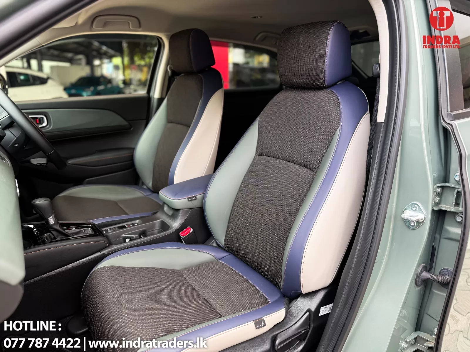 Front car interior with multicolored seats in black, gray, blue and cream; passenger door on the right is open and logo is in the corner.