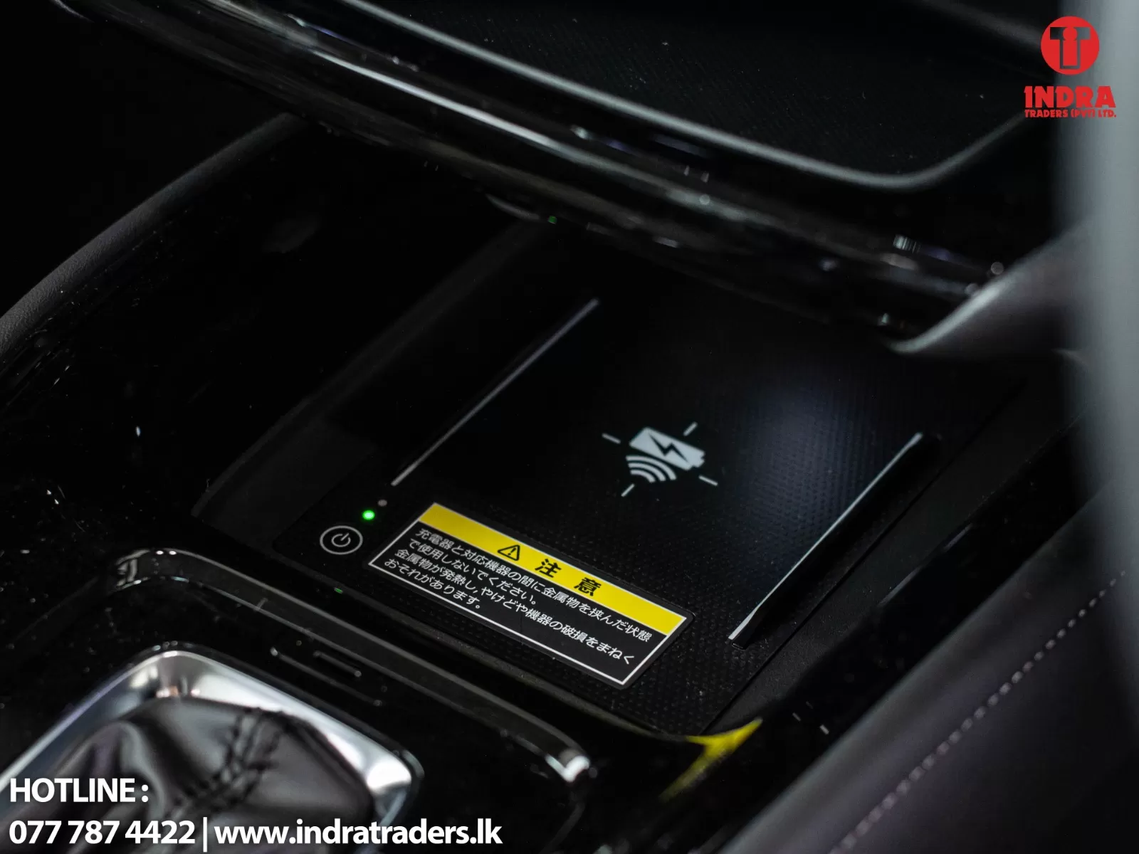 In-car wireless charging pad with a green indicator light, located in the center console, alongside a safety warning label and the Indra Traders logo in the corner.