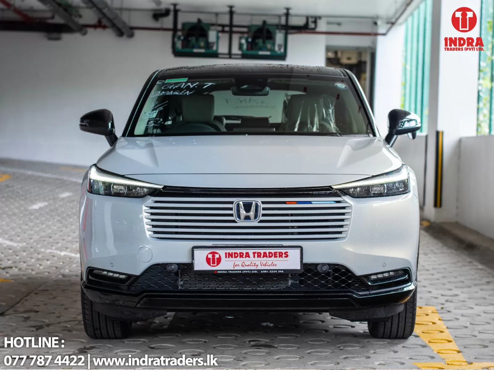 Front view of a white Honda SUV in a showroom, with Indra Traders branding on the license plate and logo in the top-right corner