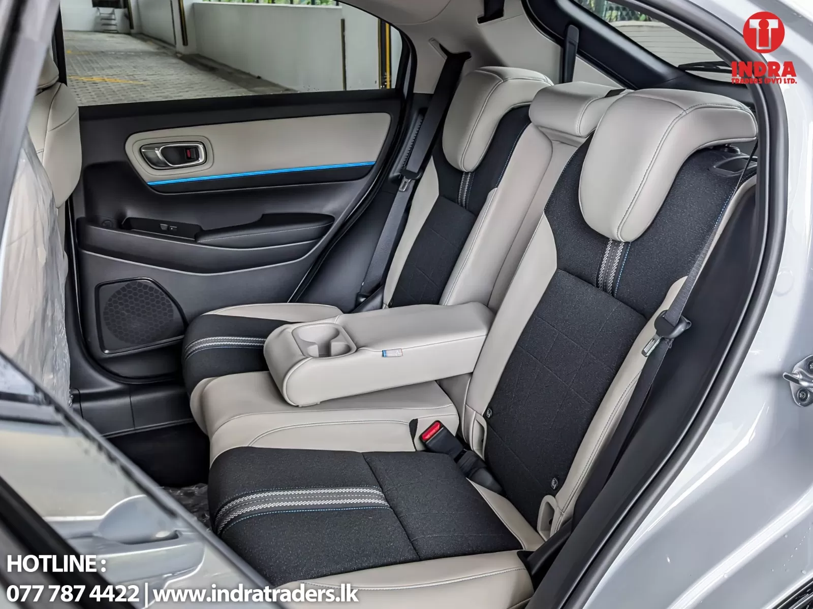 Rear car seats interior: two-tone beige and black upholstery, fold-down center armrest with cup holders, door panel with blue accent light and speaker at lower door. logo visible in corner.