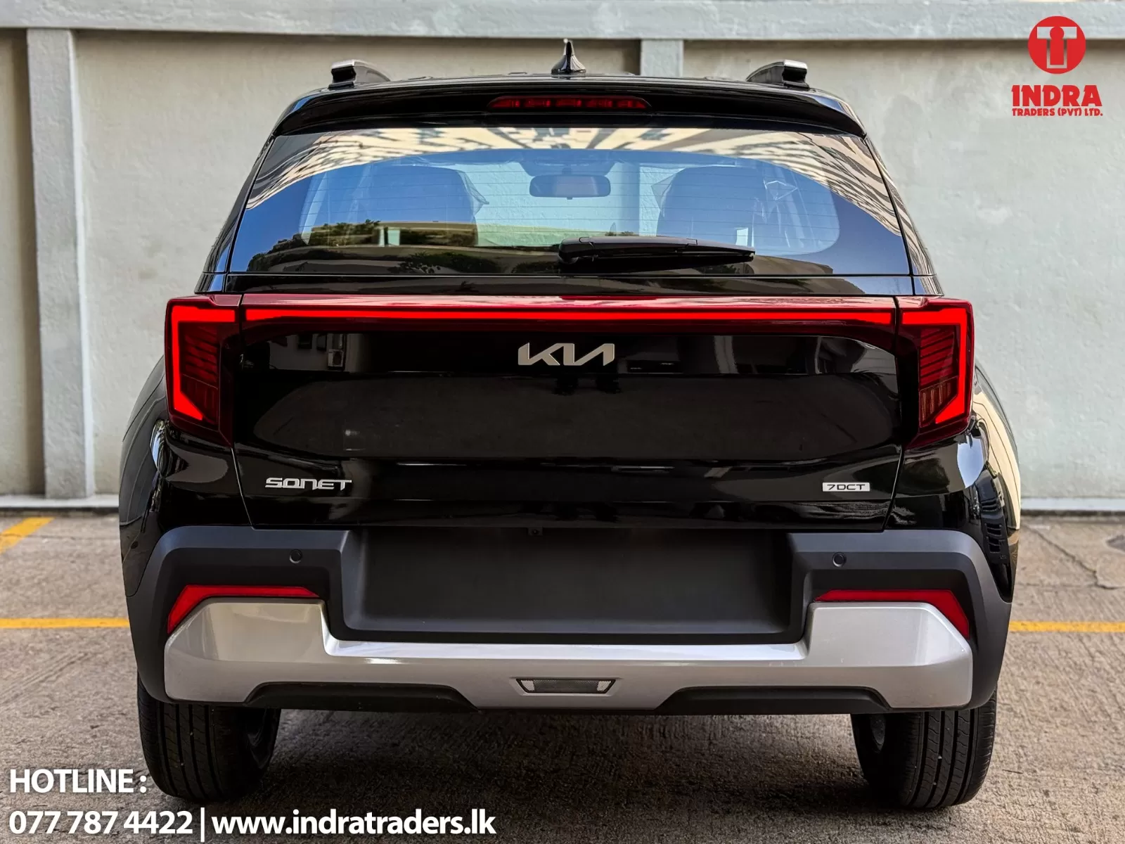 Rear view of a glossy black Kia Sonet SUV with red tail lights and 'KIA' badge, parked against a light wall. Includes Indra Traders logo in top-right and contact line at bottom.