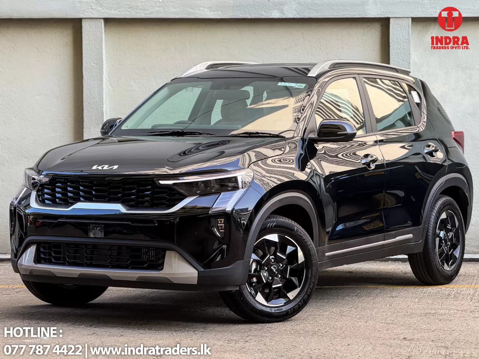 Black Kia SUV parked outdoors beside a beige wall, with Indra Traders logo in the top-right corner.