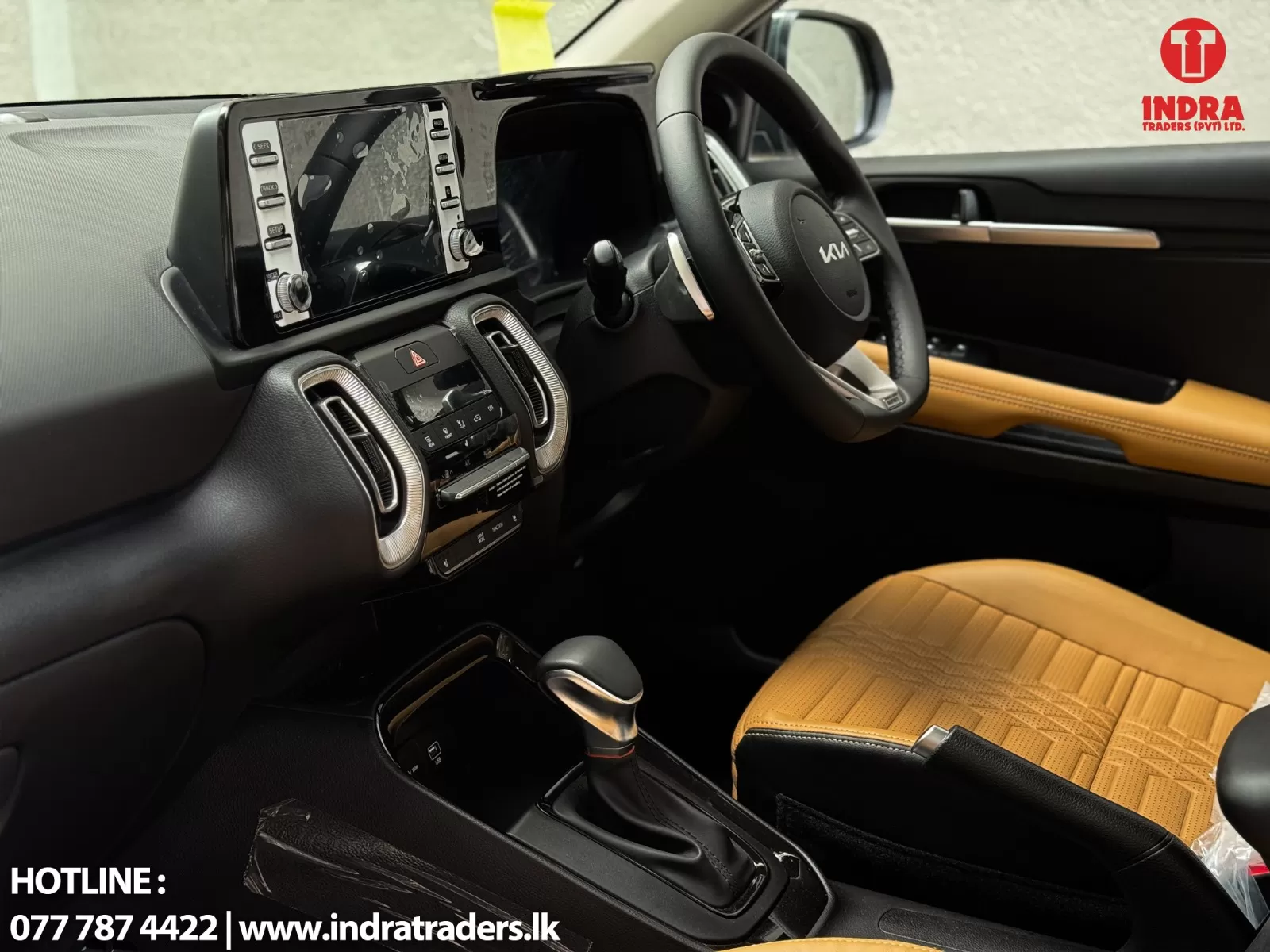 Interior of a car showing the black dashboard, center console, steering wheel, and tan leather seats with a logo in the top-right corner.