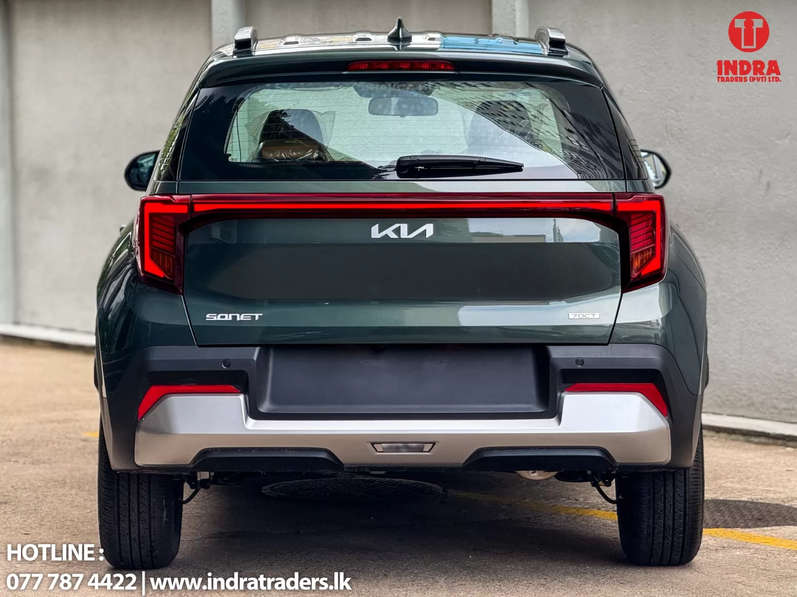 Rear view of a dark green Kia Sonet SUV parked outdoors, showing the tailgate with the Kia emblem and distinctive red taillights; Indra Traders logo in the top-right corner and hotline/website text at the bottom-left.