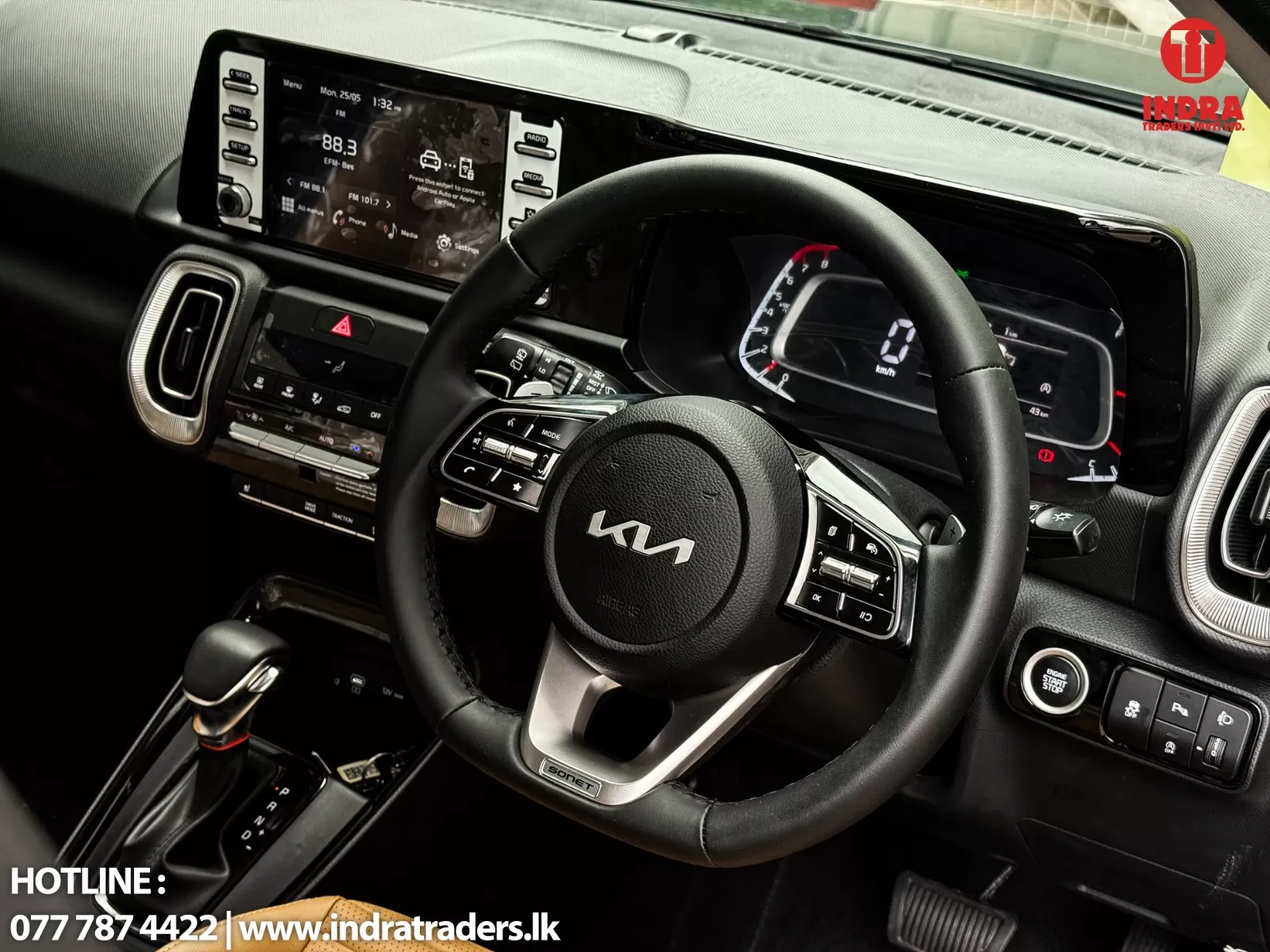 Close-up of a car interior: Kia steering wheel, digital instrument cluster, and wide center touchscreen display; dealership watermark visible in corner.
