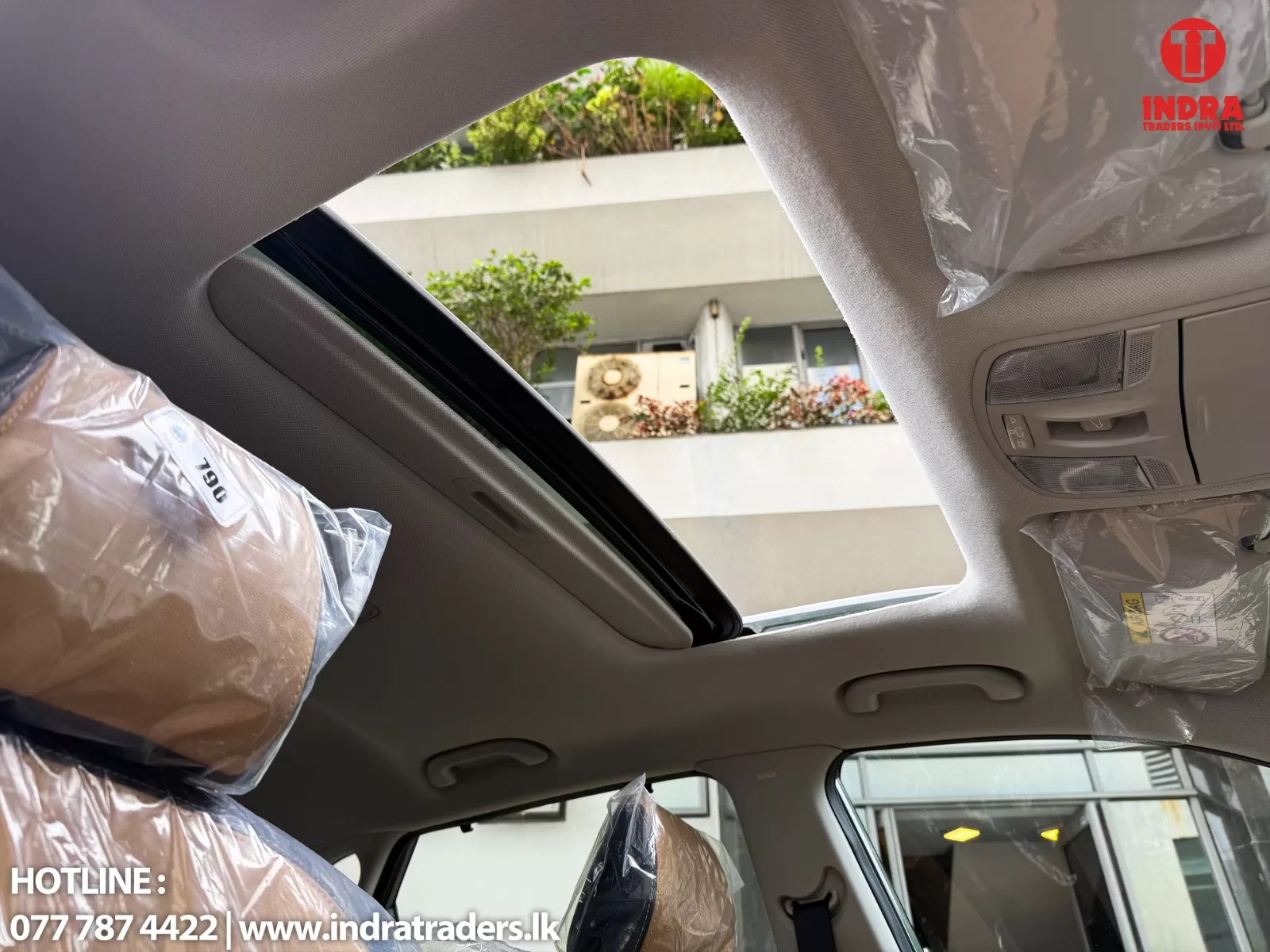 Interior of a new car with plastic-wrapped seats and an open sunroof, view of a building outside through the roof opening.