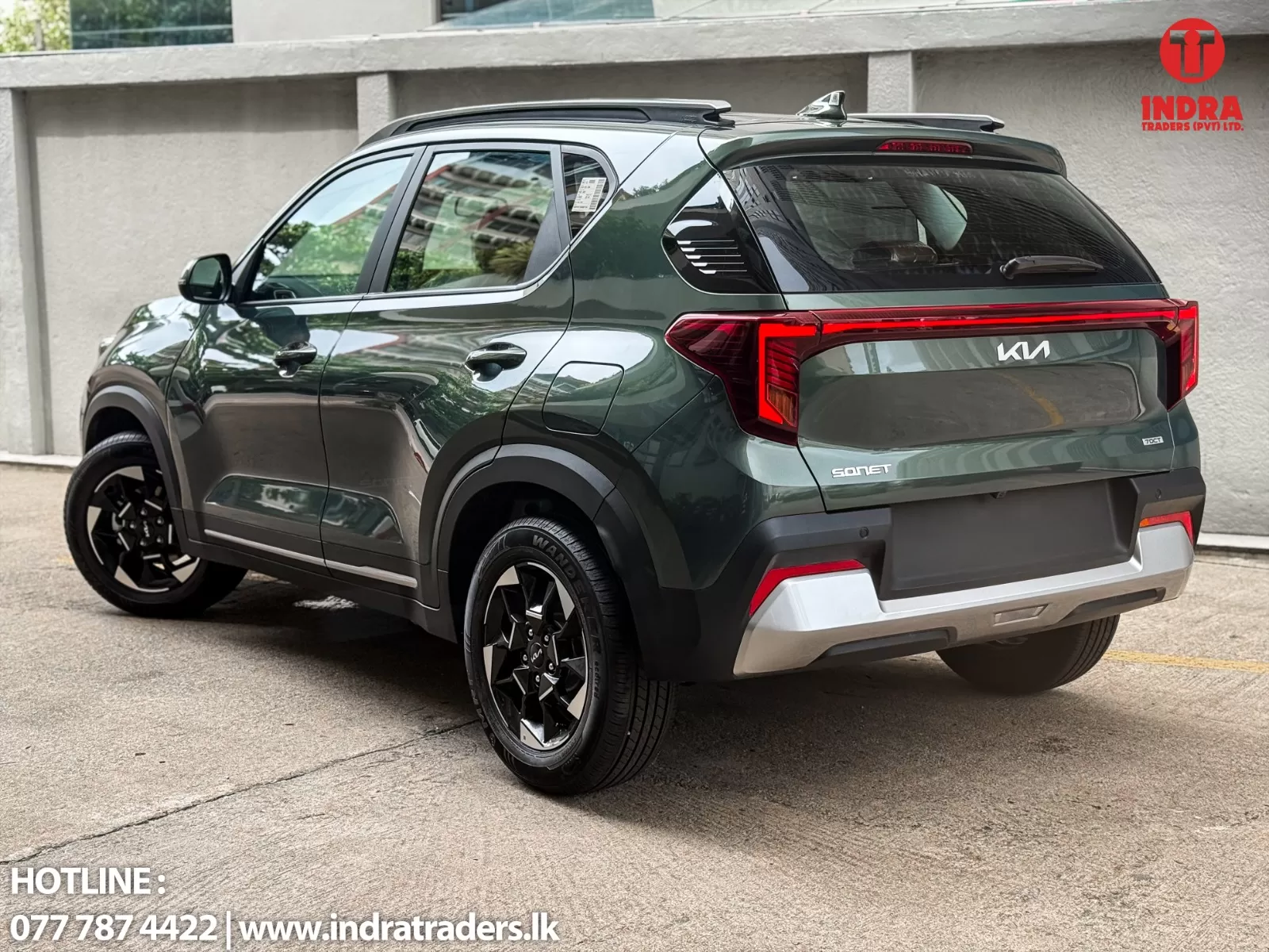 Dark green Kia Sonet SUV rear three-quarter view, parked outdoors; dealership logo top-right and hotline text bottom-left.
