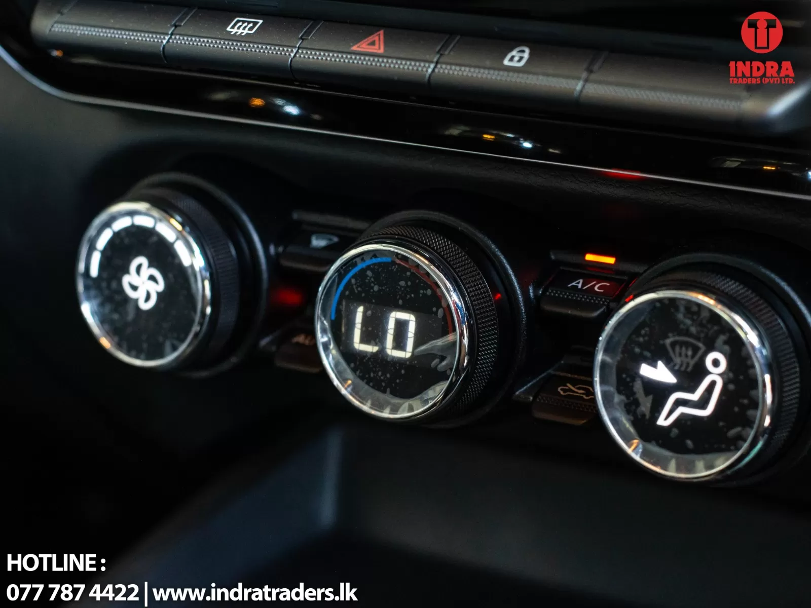 Car climate control panel with three chrome dials: left fan speed, center low temperature readout displaying 'LO', right airflow/seat symbol; watermark visible in top-right corner.