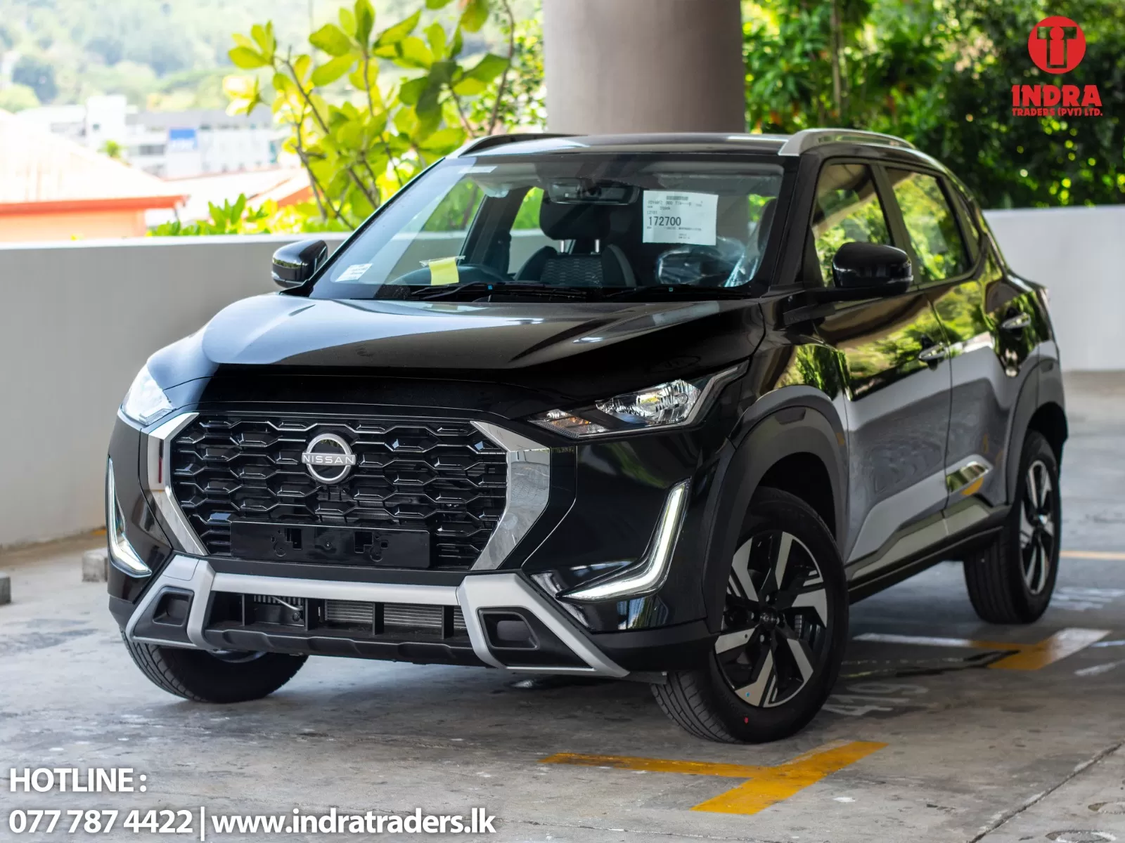 Front three-quarter view of a glossy black Nissan SUV in a parking area, with Indra Traders logo visible in the top-right corner.