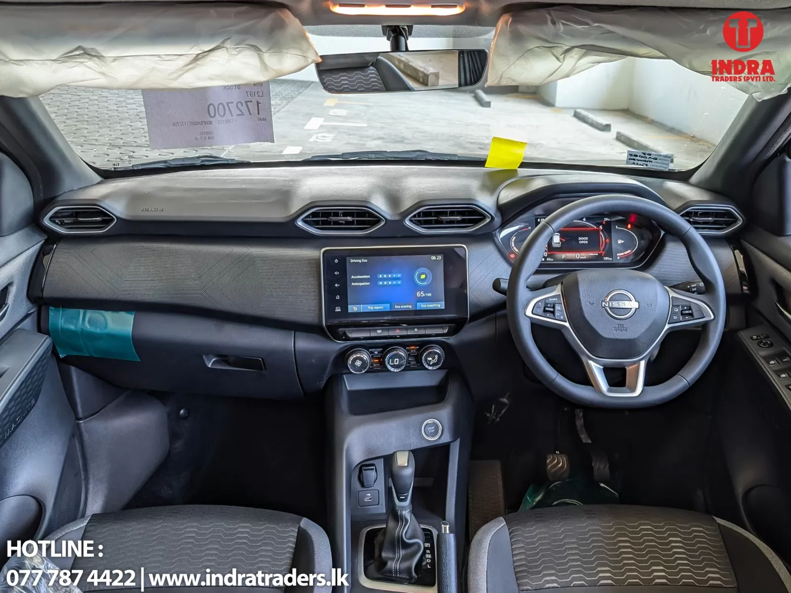 Right-hand drive car interior with steering wheel, central touchscreen, and climate controls visible; dashboard and windshield in view, Indra Traders watermark in top-right corner
