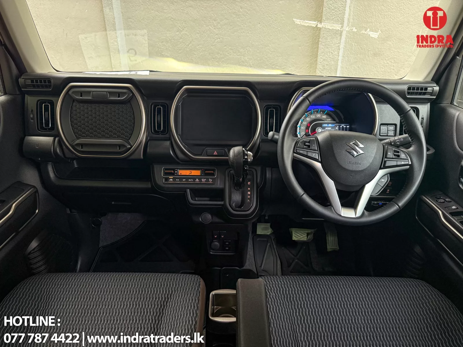 Interior of a dark car dashboard featuring a Suzuki steering wheel, large central touchscreen, round instrument cluster, gear selector, and Indra Traders watermark along the windshield.