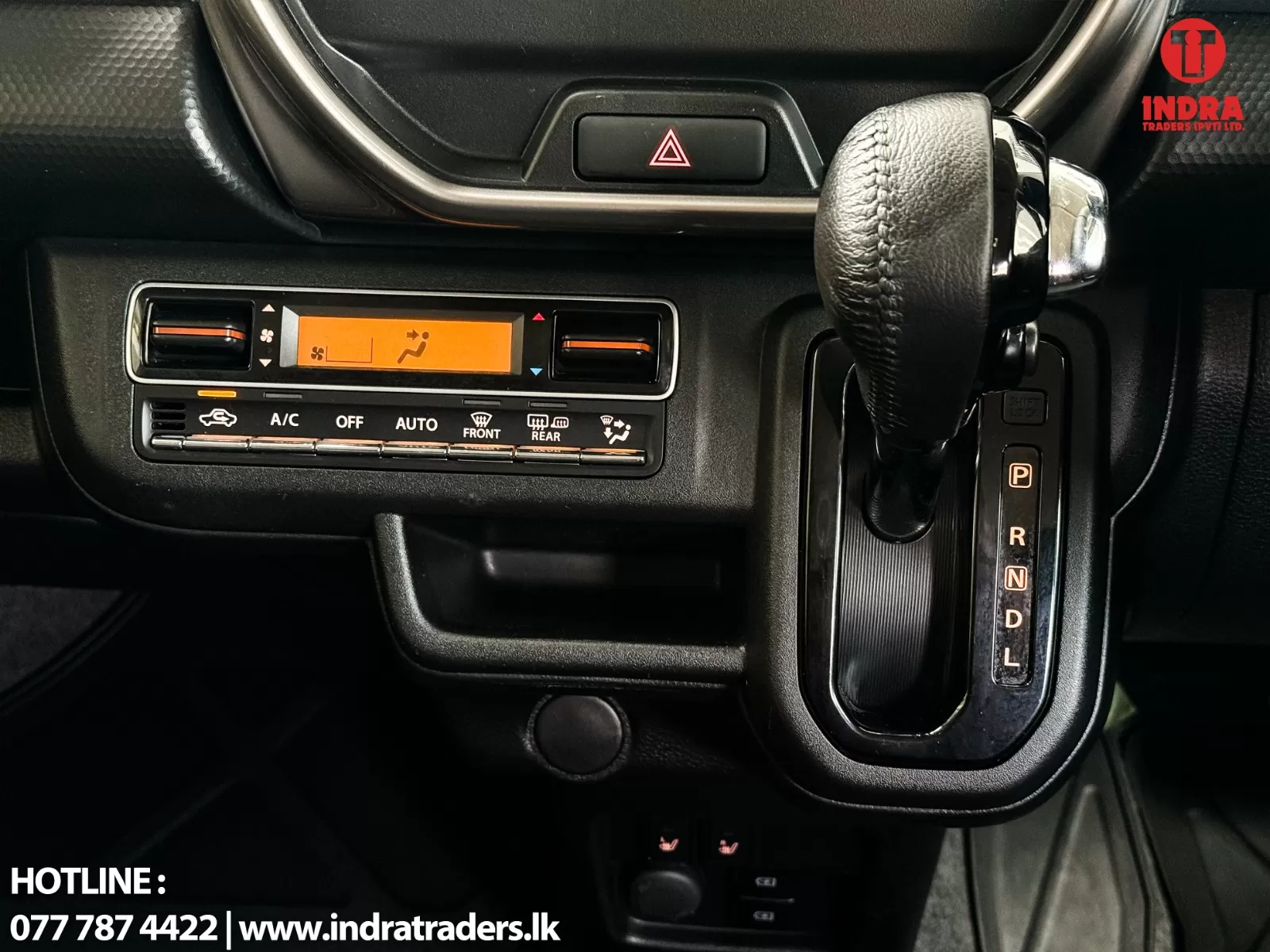 Car interior showing climate control panel with orange display and gear shifter on the right; hazard button above.