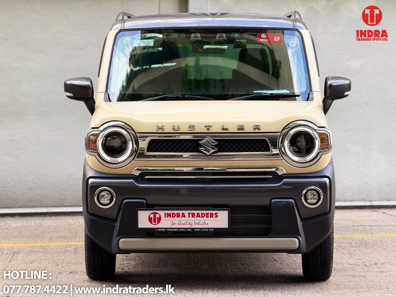 Front view of a beige Suzuki Hustler SUV parked, showing large round headlights and chrome grille; Indra Traders branding visible on the right.
